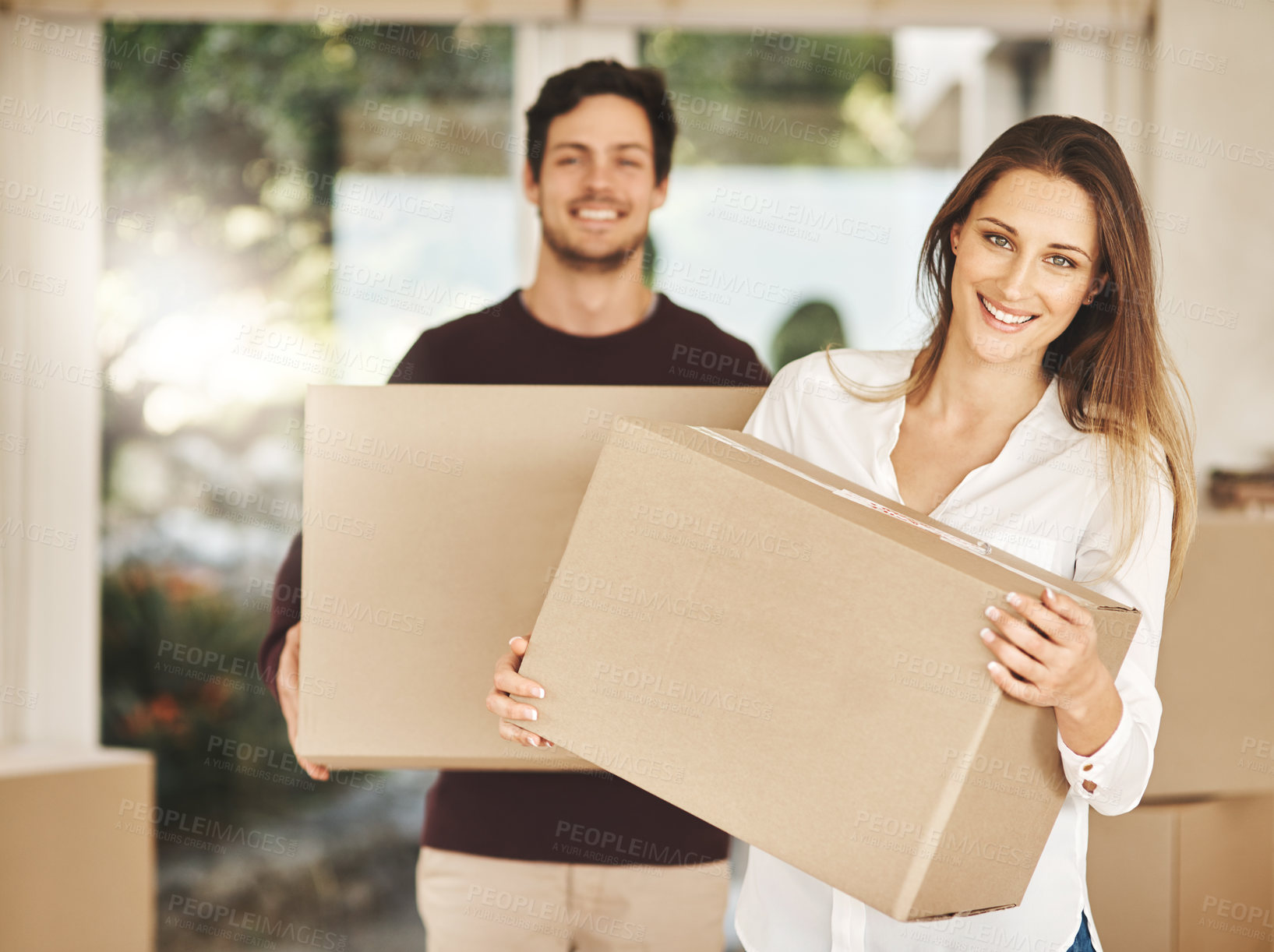 Buy stock photo Portrait of a smiling young couple carrying boxes while moving into their new home