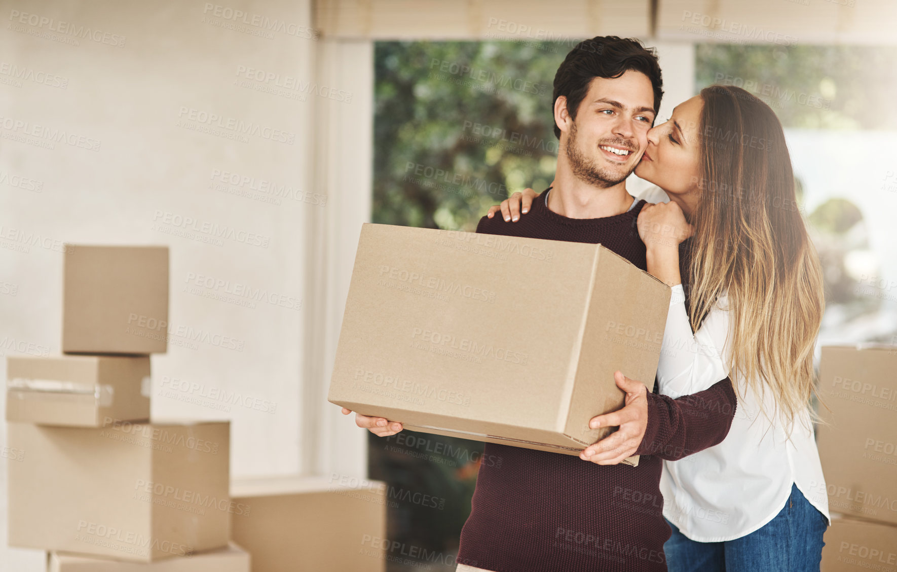 Buy stock photo Shot of a smiling young couple kissing while carrying boxes on moving day