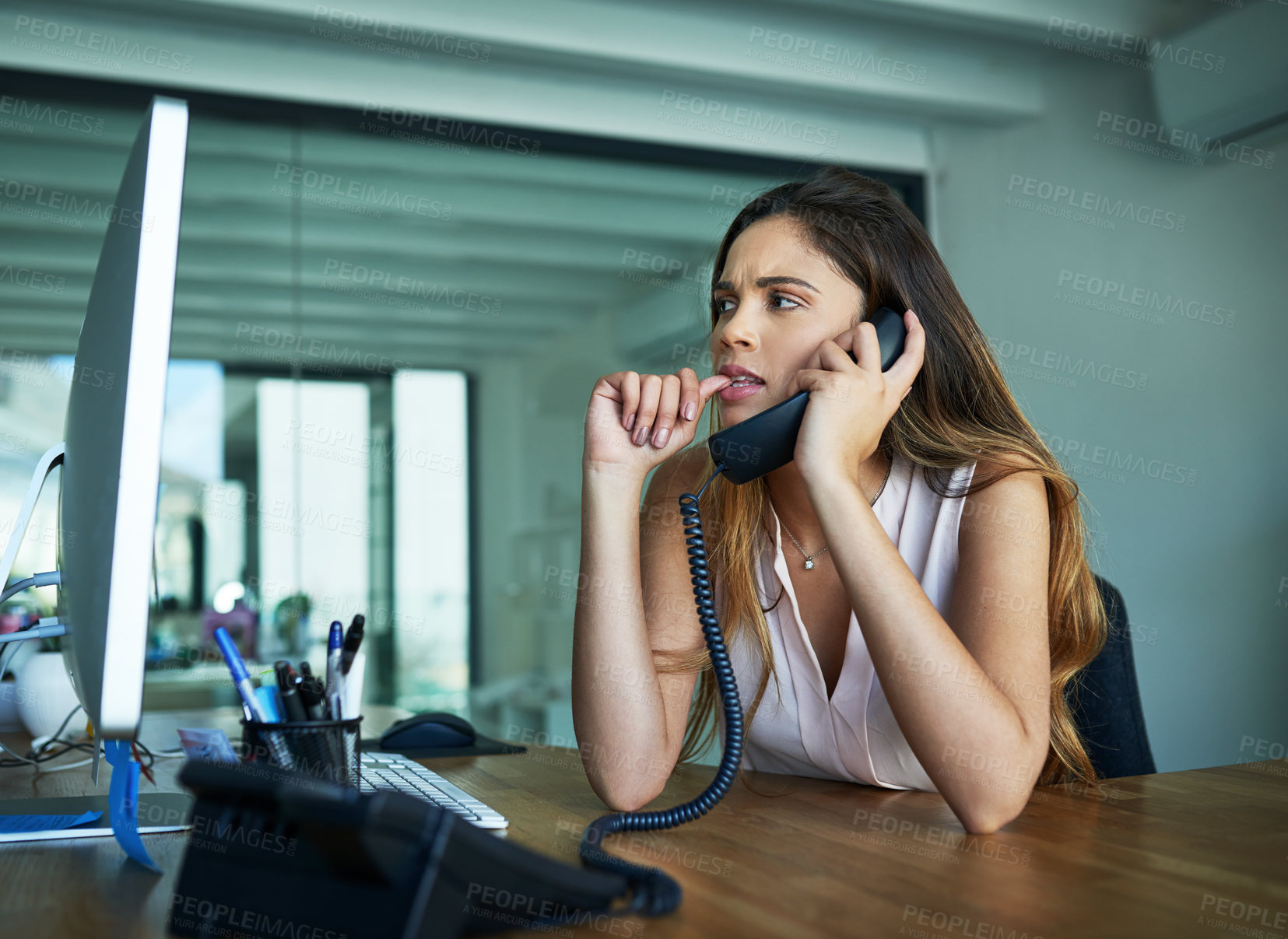 Buy stock photo Shot of a young businesswoman biting her nails while talking on a phone in an office