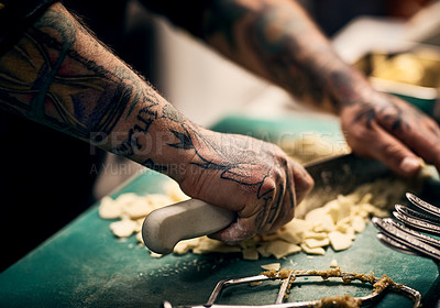 Buy stock photo Closeup of a unrecognisable chef's tattooed hands cutting up vegetables with a knife on a board in a kitchen