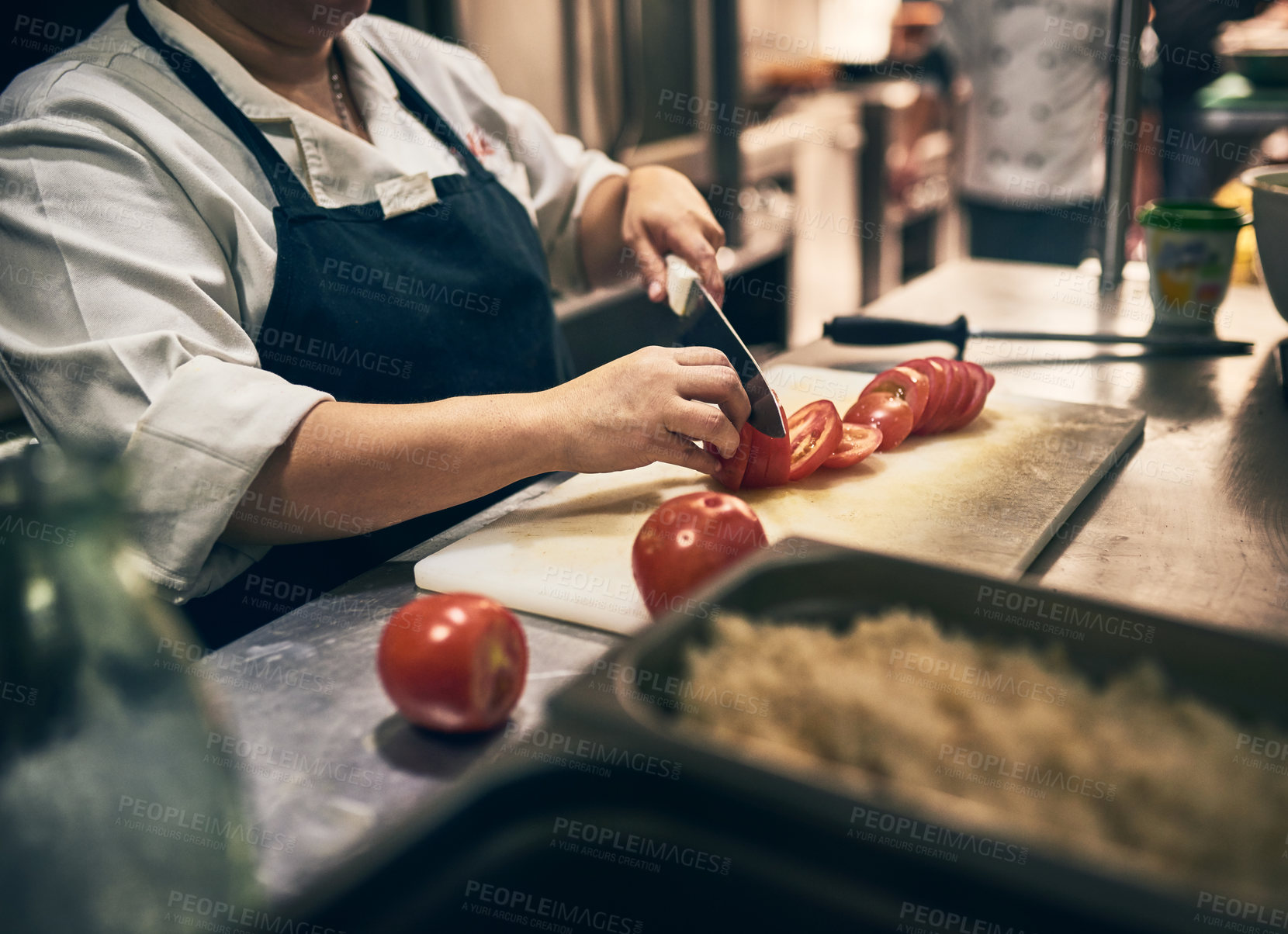 Buy stock photo Shot of a unrecognisable chef cutting up tomatoes with a knife on a board in a kitchen