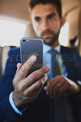 Buy stock photo Shot of a focused young businessman holding his cellphone while being seated in the back off a car
