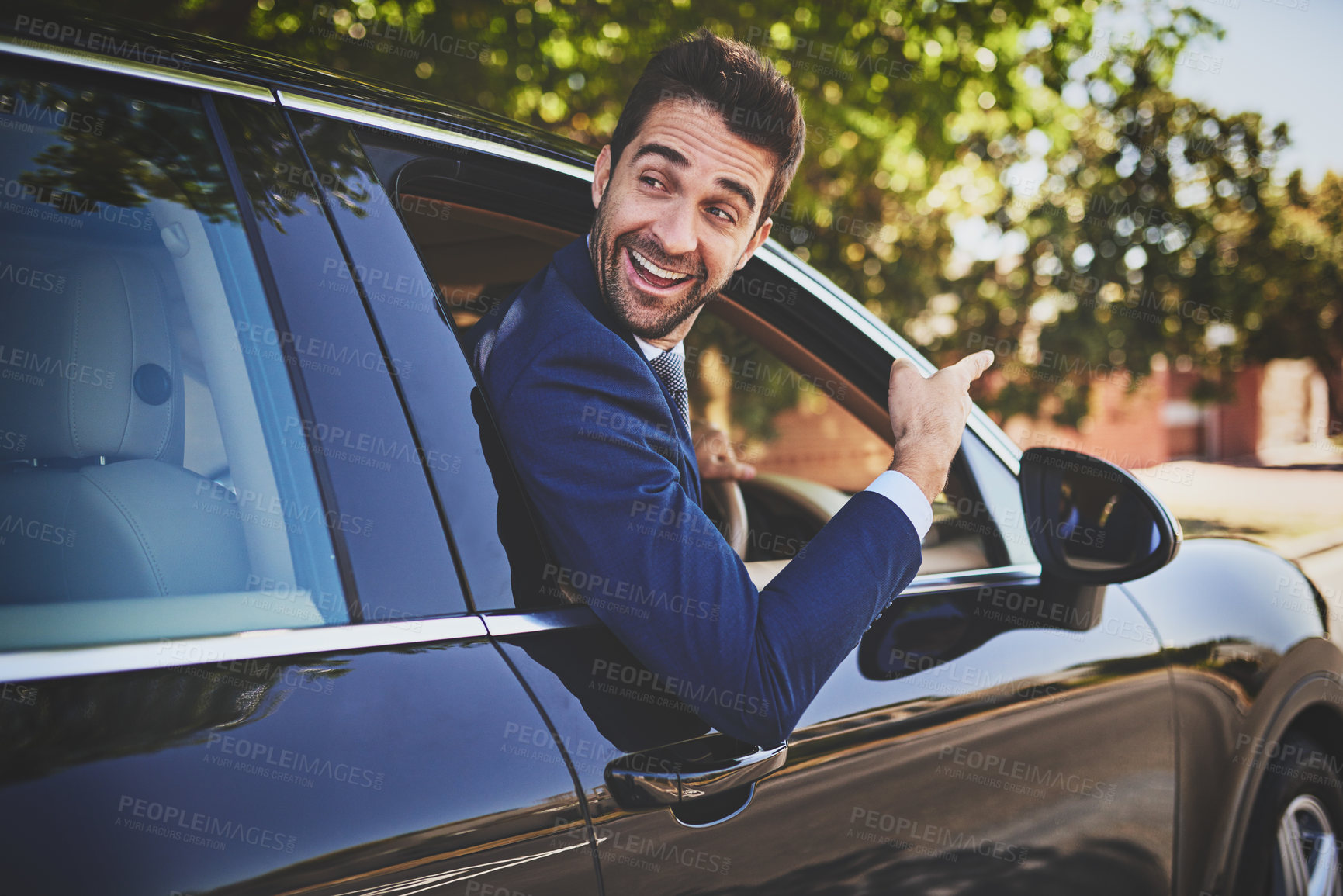 Buy stock photo Shot of a cheerful young businessman hanging out of a car window and pointing with his hand towards the front of his car