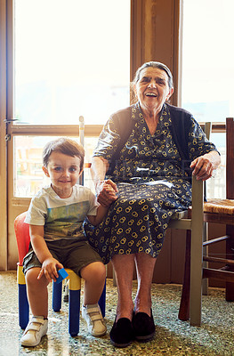 Buy stock photo Portrait of a cheerful little boy sitting next his great grandmother while looking into the camera at home