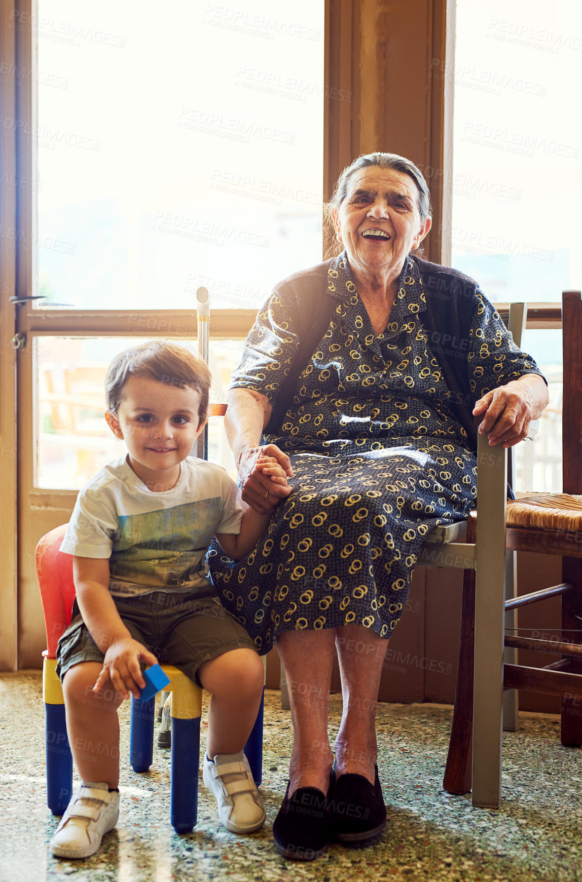 Buy stock photo Portrait of a cheerful little boy sitting next his great grandmother while looking into the camera at home