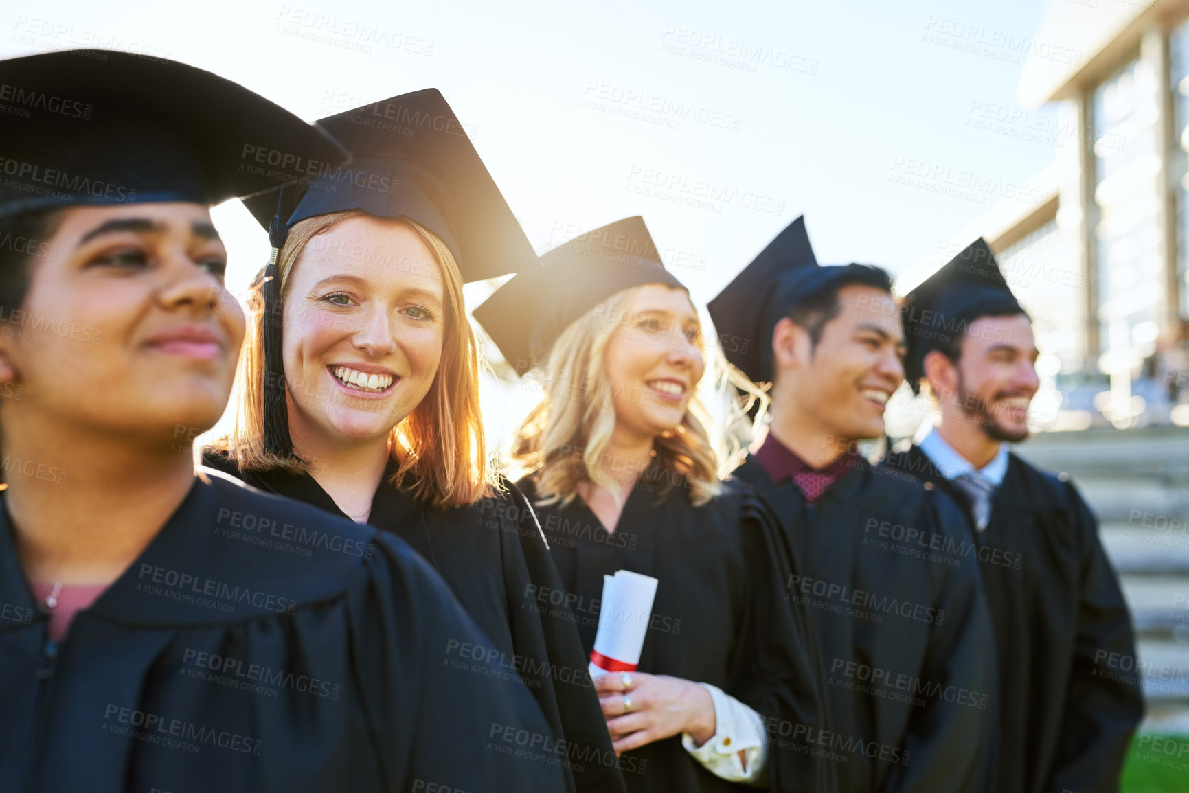 Buy stock photo Shot of a group of students standing in a line on graduation day