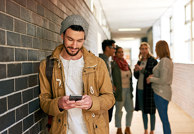 Buy stock photo Shot of a young male university student standing in a campus corridor with his classmates in the background