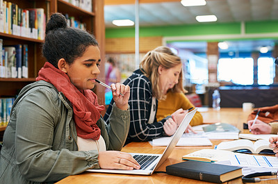 Buy stock photo Shot of a focused young female student working on her laptop and studying inside of a library