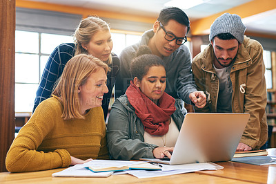 Buy stock photo Shot of a cheerful young group of students working together using a laptop to study for exams inside of a library