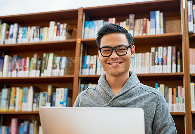 Buy stock photo Portrait of a cheerful young man busy working on his laptop and studying while being seated inside of a library