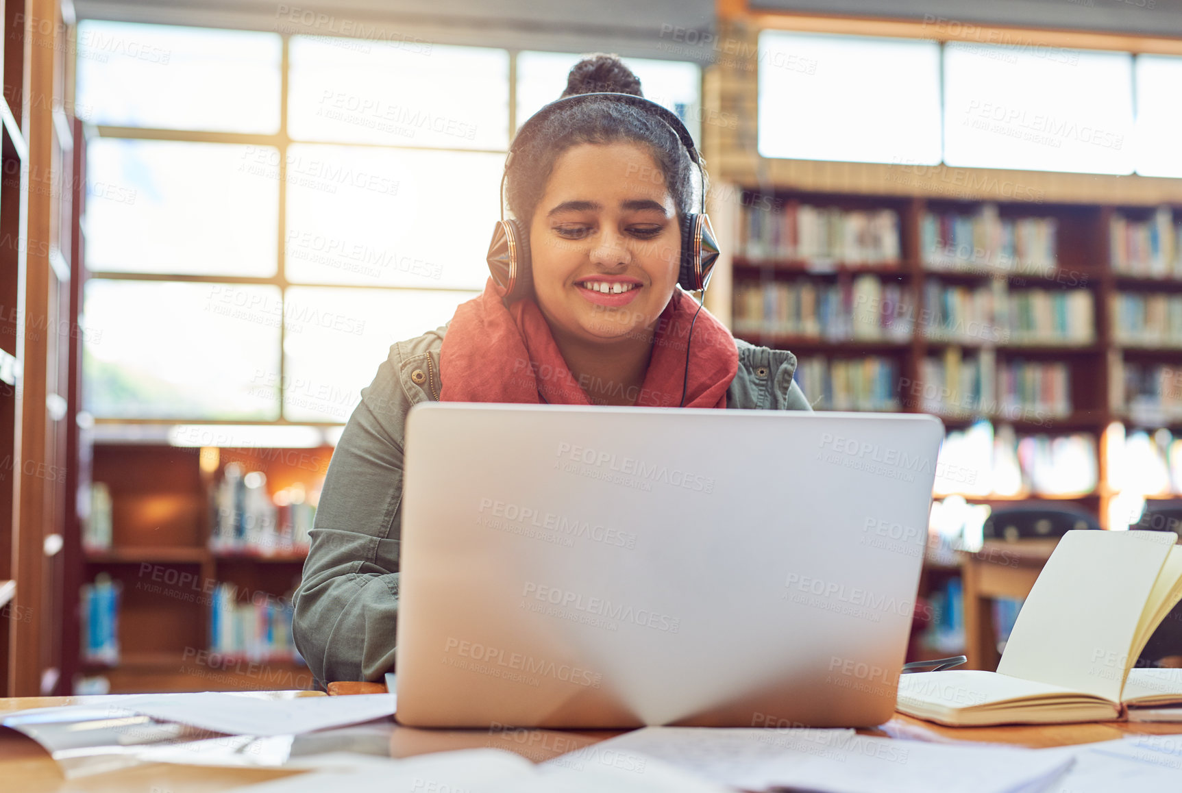 Buy stock photo Shot of a cheerful young female student working on a laptop while listening to music with her headphones inside of a library