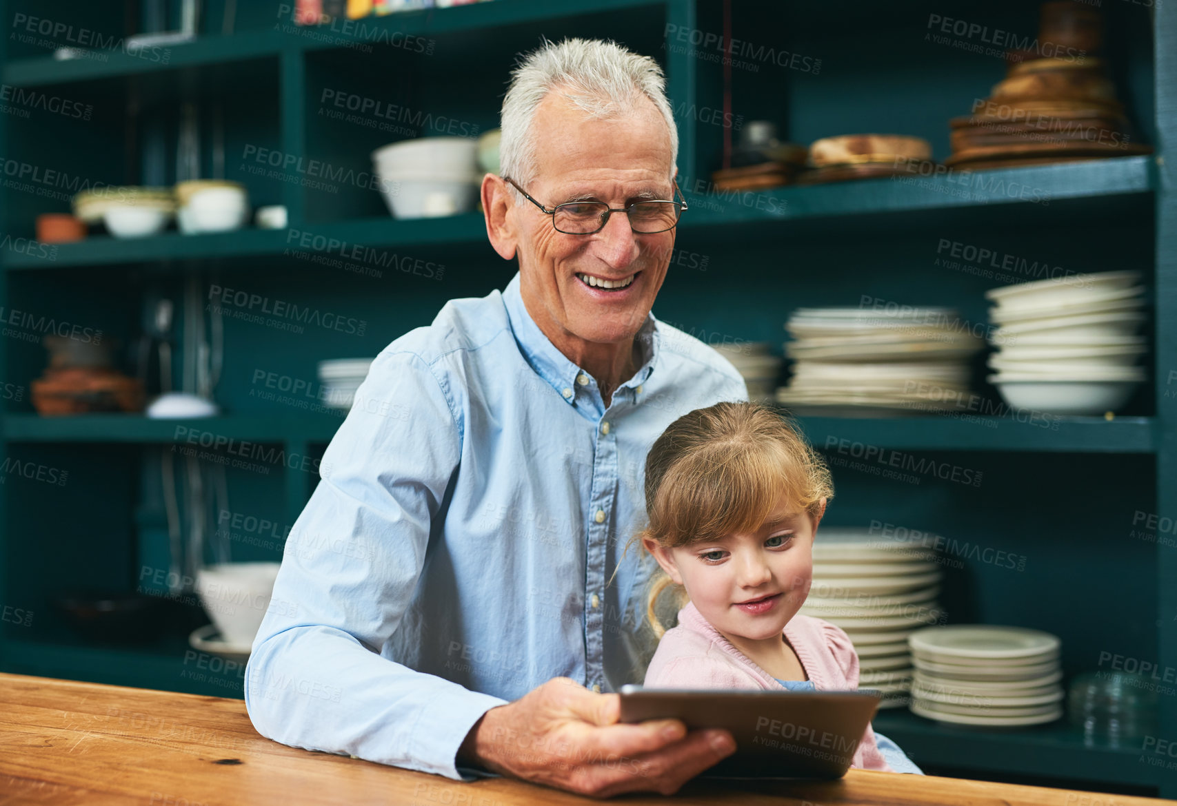 Buy stock photo Cropped shot of a cheerful elderly man and his little grand daughter playing around on a digital tablet next to a table at home