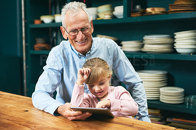 Buy stock photo Cropped shot of a cheerful elderly man and his little grand daughter playing around on a digital tablet next to a table at home
