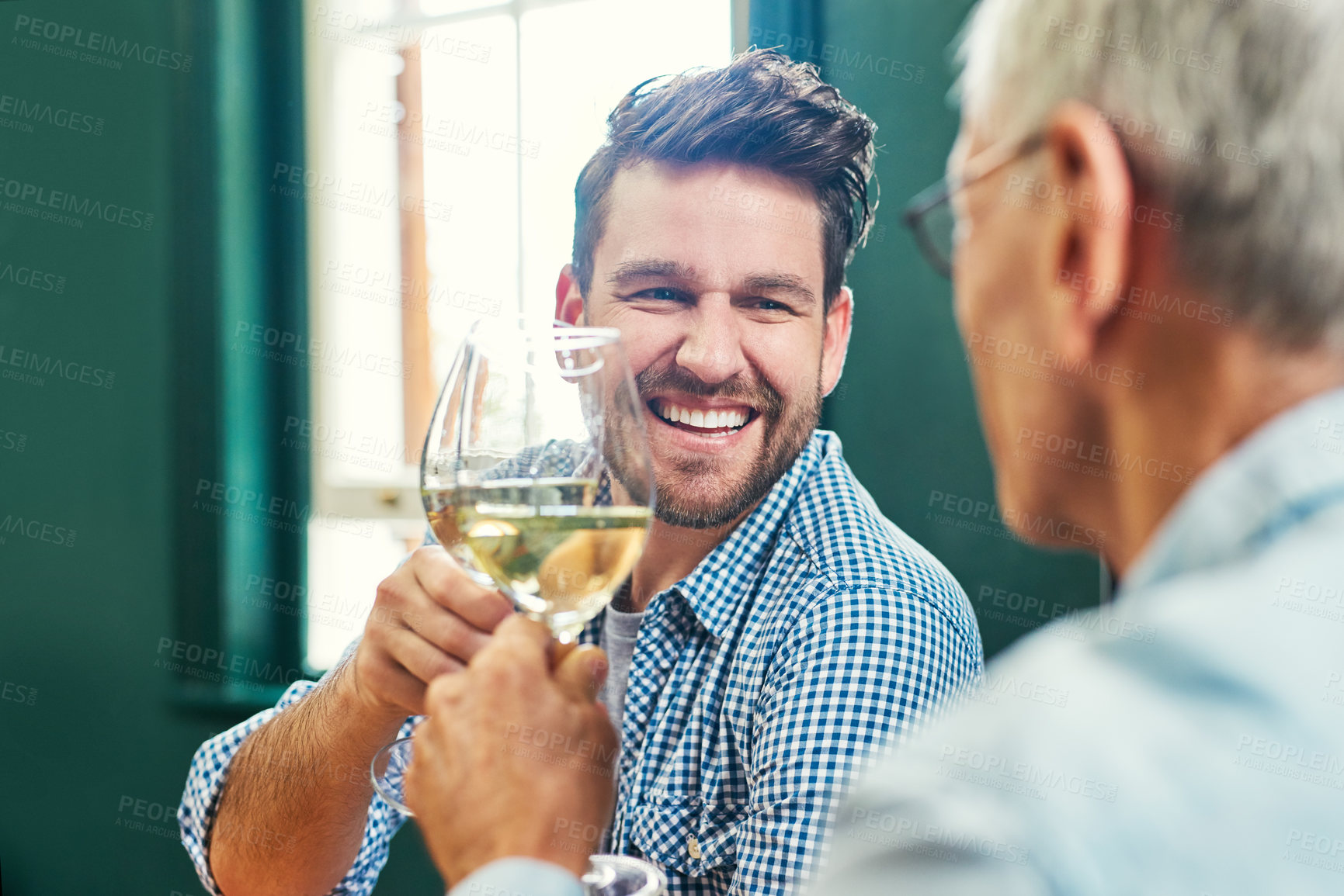 Buy stock photo Shot of a cheerful young man and his mature father sharing a celebratory toast with wine glasses at home