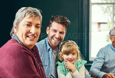Buy stock photo Portrait of a cheerful family sitting together around a dinner table while looking at the camera at home
