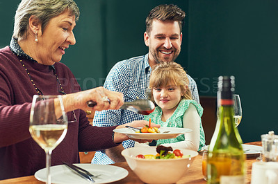 Buy stock photo Shot of a cheerful elderly woman dishing up food for her granddaughter around a dinner table at home