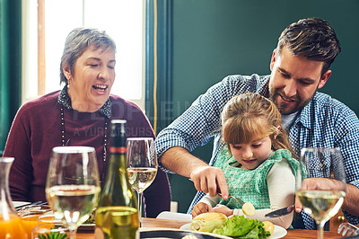 Buy stock photo Shot of a cheerful young man helping to cut his daughter's food while being seated around a dinner table at home
