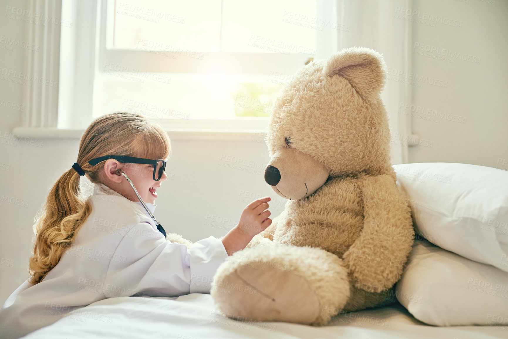 Buy stock photo Shot of an adorable little girl dressed up as a doctor and examining a teddy bear with a stethoscope