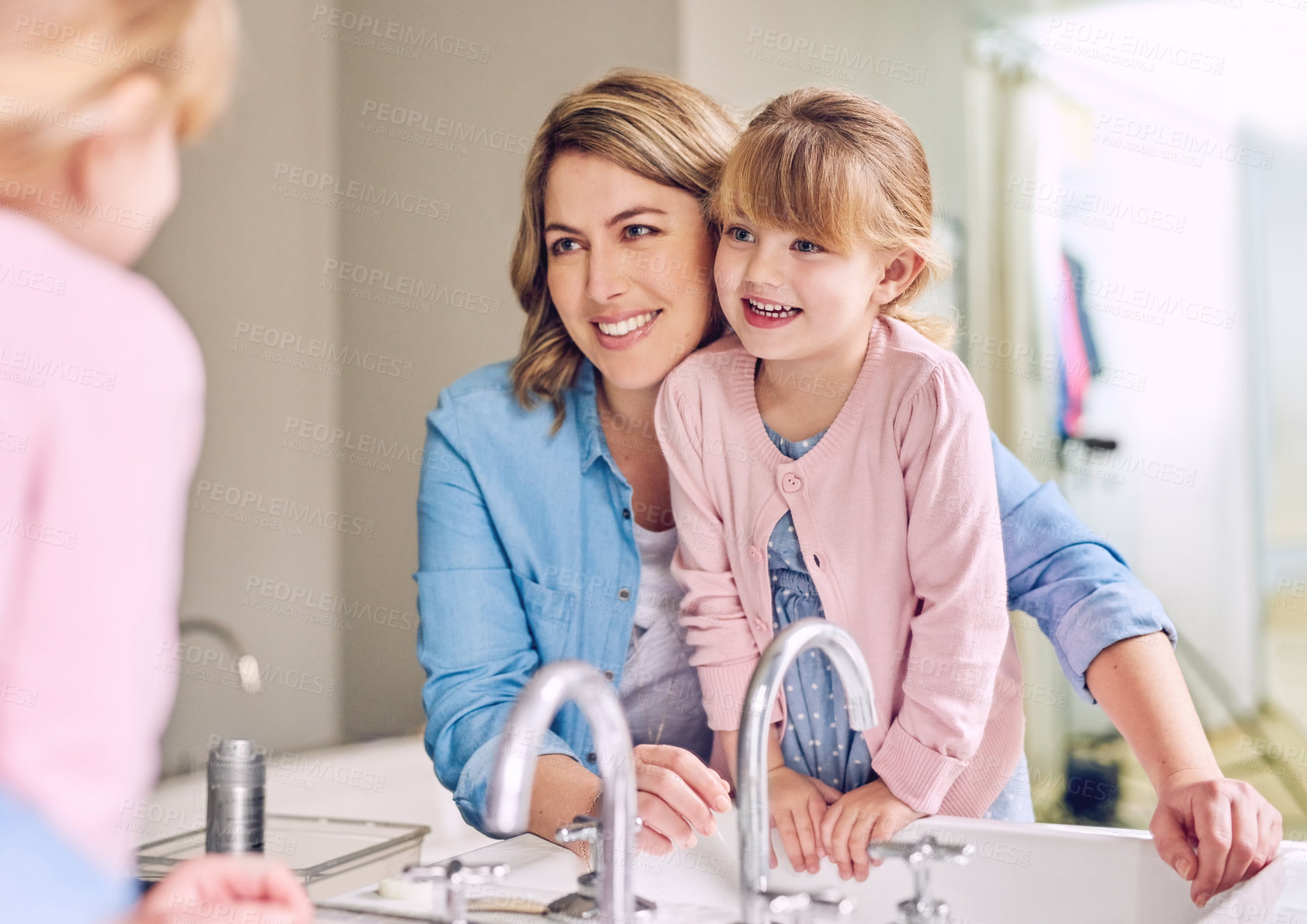 Buy stock photo Shot of a cheerful young  mother and her daughter washing hands while looking at their reflection in a mirror