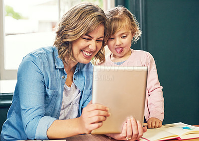 Buy stock photo Shot of a cheerful young mother and her young little daughter playing around on a digital tablet at home