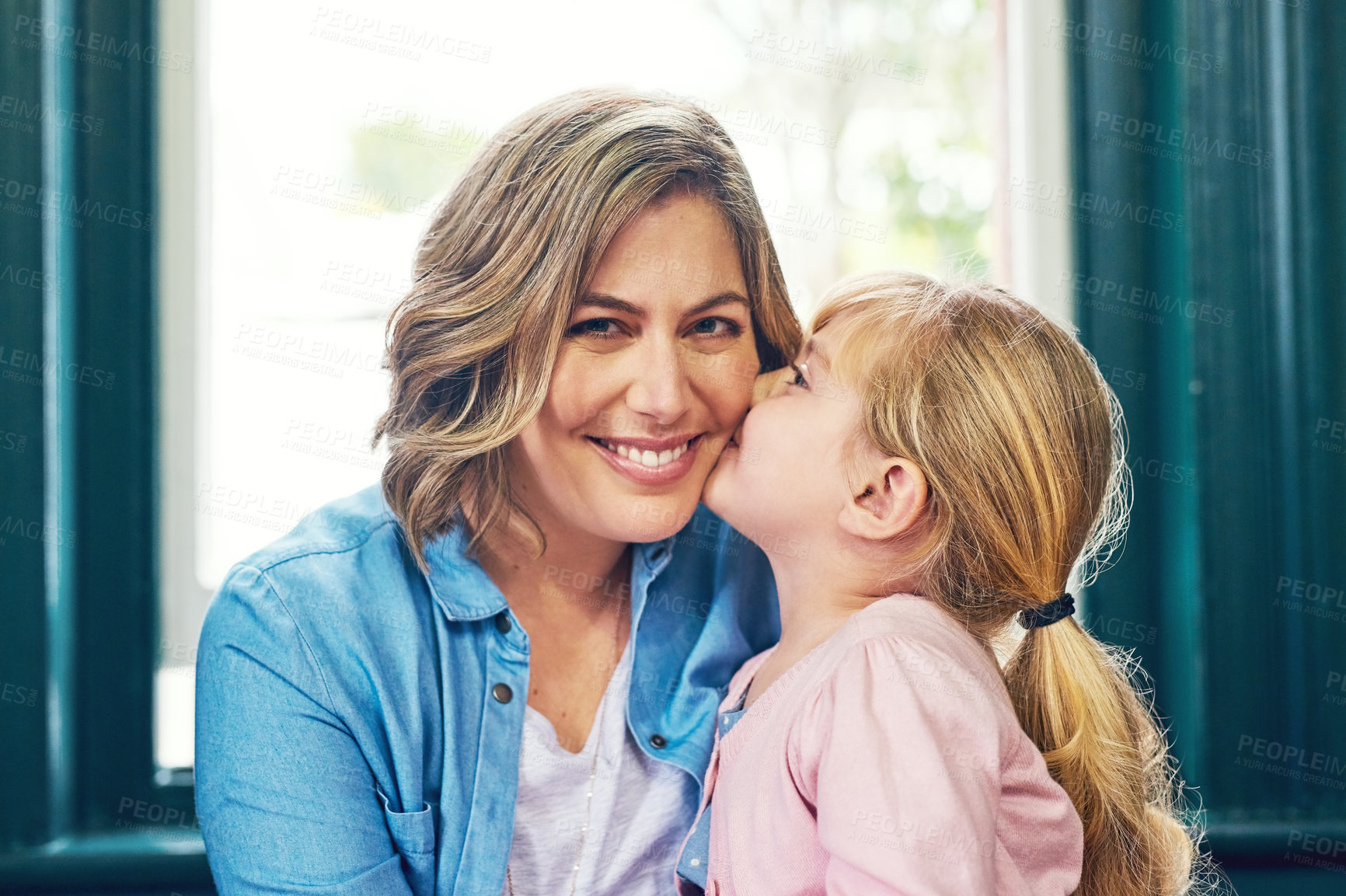 Buy stock photo Portrait of a cheerful young mother receiving a kiss on the cheek by her young little daughter