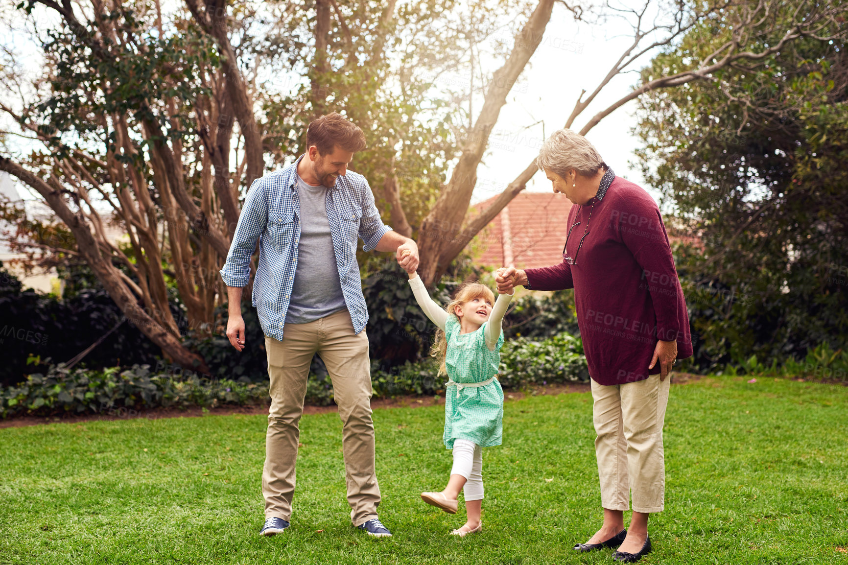 Buy stock photo Holding hands, daughter swinging with dad and granny in garden of home together for bonding or visit. Fun, love or smile with family of girl, parent and senior woman outdoor in nature for excitement