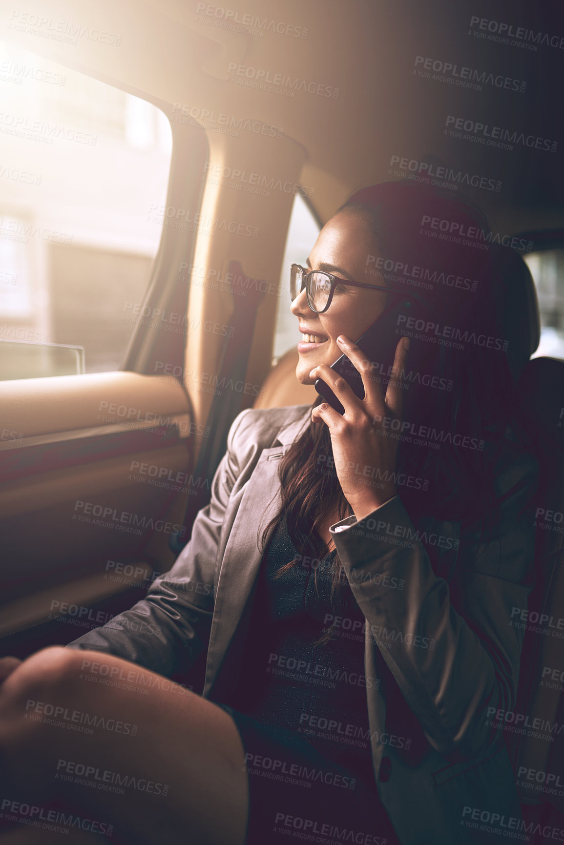Buy stock photo Shot of a young businesswoman talking on a cellphone in the backseat of a car