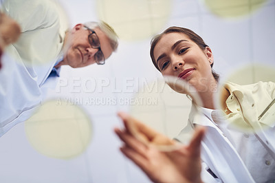 Buy stock photo Low angle shot of two scientists conducting an experiment in a lab