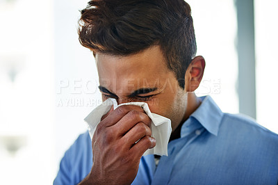 Buy stock photo Shot of a young businessman blowing his nose at work