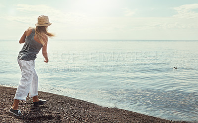 Buy stock photo Beach, water and woman skipping rocks outdoor in summer for hobby, leisure or vacation from back. Coast, ocean and sky with person throwing stone into sea or nature for break, holiday or weekend trip