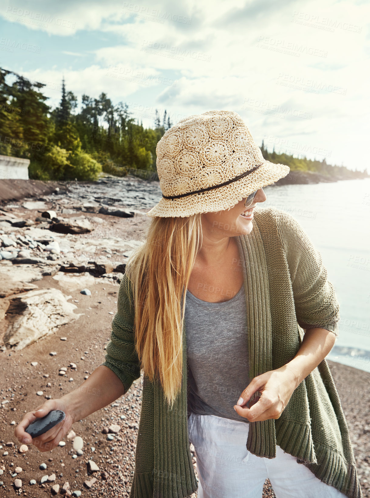 Buy stock photo Throw pebbles, lake and woman with smile, nature and weekend break with getaway trip. Outdoor, tourism and person with summer holiday, playing and river with game, hat and rocks with vacation
