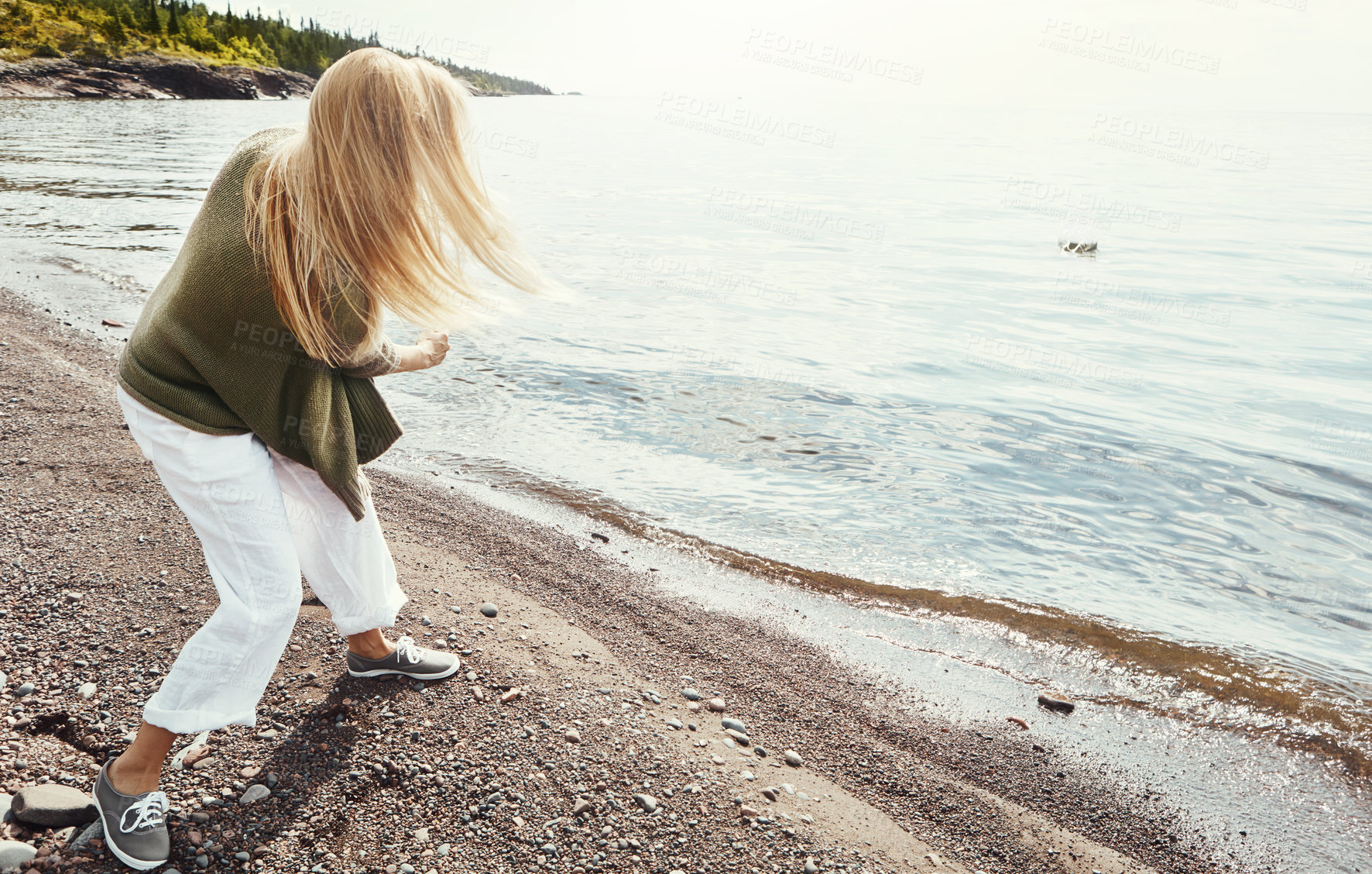 Buy stock photo Beach, coast and woman skipping stone outdoor in summer for hobby, leisure or vacation from back. Earth, ocean and person throwing rocks into sea or water for break, holiday or weekend trip on sky