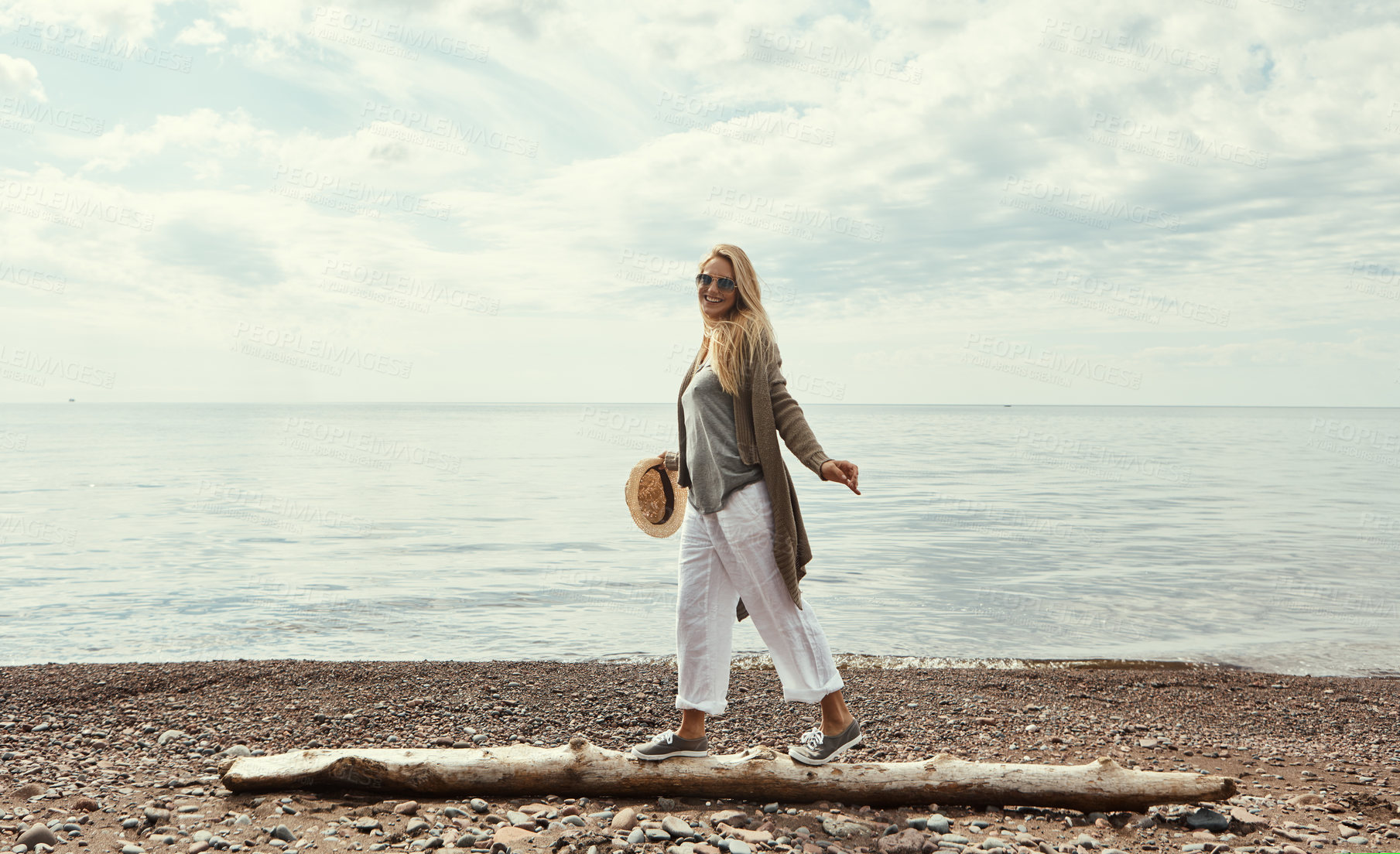 Buy stock photo Shot of a young woman walking along a log at a lake