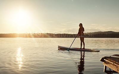 Buy stock photo Lake, sunset and woman on paddle board for relax, water sports and vacation on river for tourism. Sunlight, summer and holiday in Germany for adventure and balance practice, swimsuit and travel