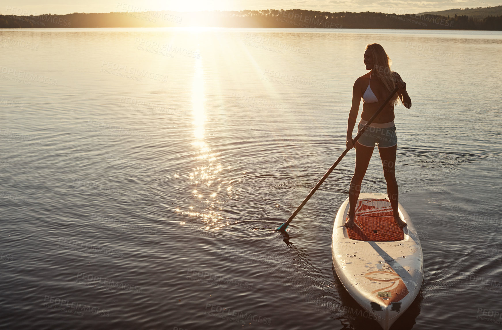 Buy stock photo Lake, sunset and woman on paddle board for relax, water sports and vacation on river for tourism. Sunlight, summer and holiday in Germany for female person, swimsuit and travel fitness for adventure