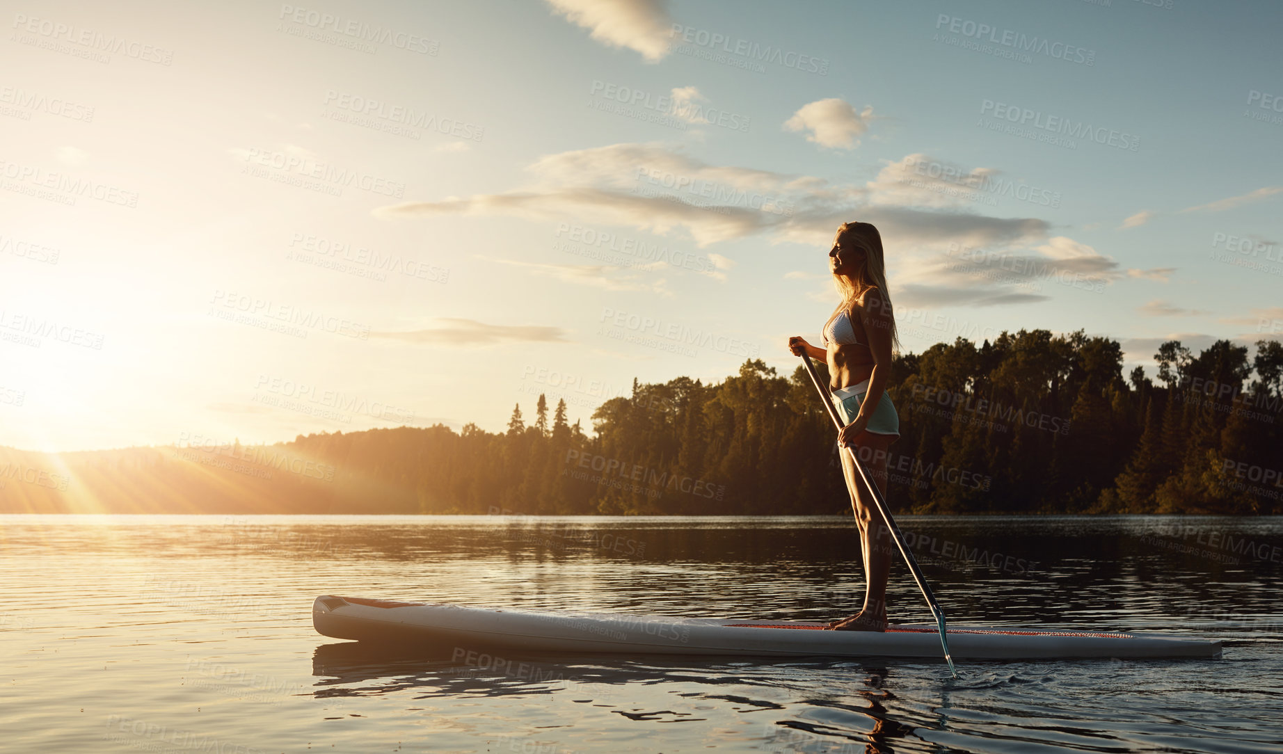 Buy stock photo Lake, sunset and woman on paddle board with trees, water sport and vacation on river for tourism. Exercise, woods or holiday in Germany for female person, swimsuit or travel fitness for adventure
