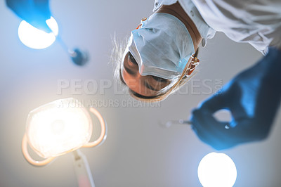 Buy stock photo Low angle shot of a focused young female dentist wearing a surgical mask while attempting to work on a patient's teeth