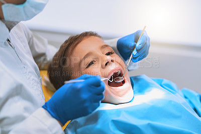 Buy stock photo Shot of a young little boy lying down on a dentist chair while getting a checkup from the dentist