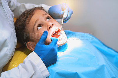 Buy stock photo Shot of a young little boy lying down on a dentist chair while getting a checkup from the dentist