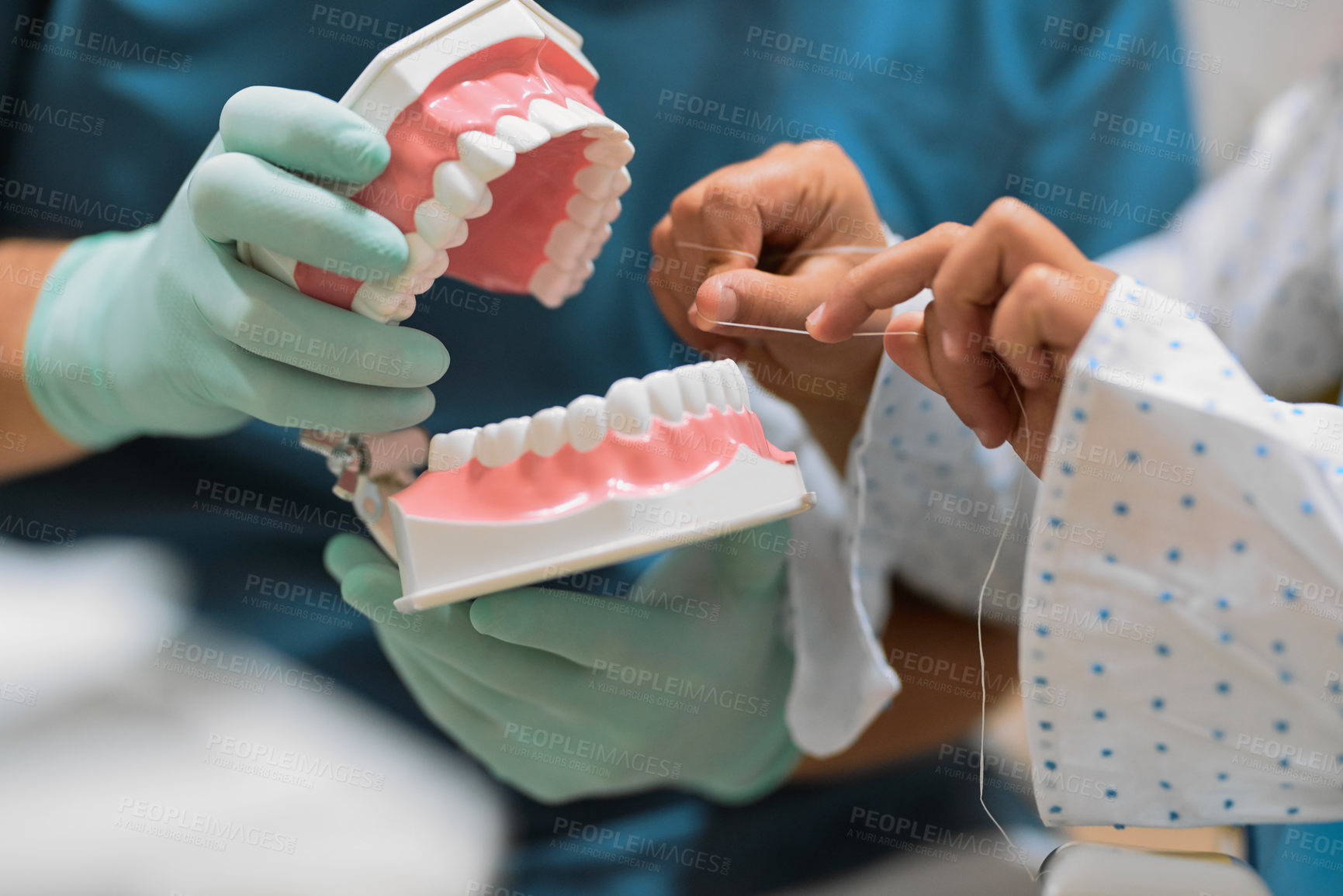 Buy stock photo Shot of a unrecognizable dentist holding a pair of artificial gums and teeth while a young little patient flosses it