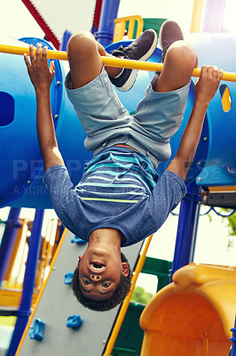 Buy stock photo Shot of a young boy hanging upside down on a jungle gym in the park