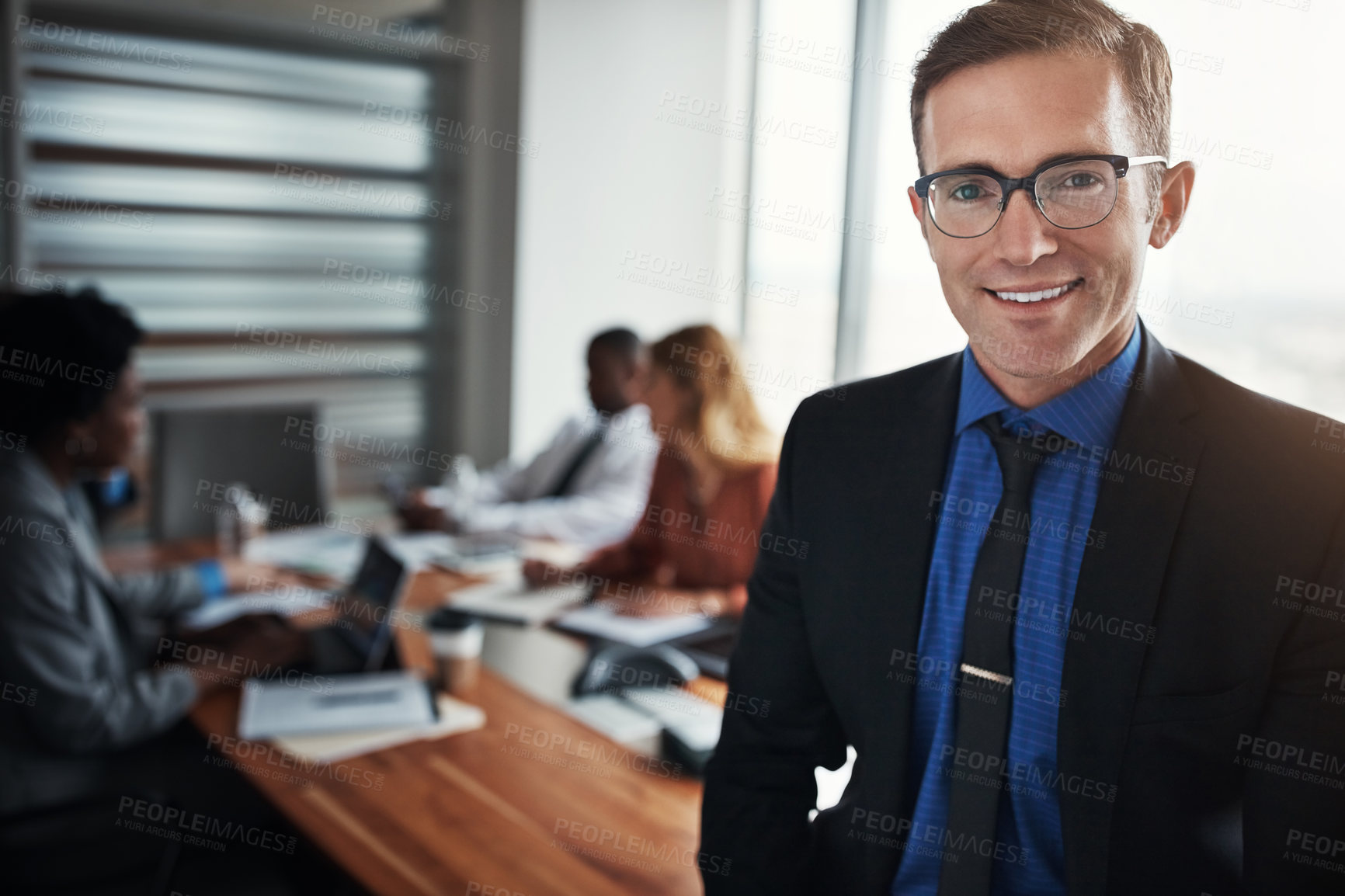 Buy stock photo Portrait of a confident businessman standing in an office with his colleagues in the background