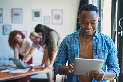 Buy stock photo Shot of a young man using a digital tablet with his team in the background of a modern office