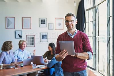 Buy stock photo Shot of a mature man using a digital tablet with his team in the background of a modern office
