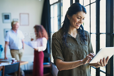 Buy stock photo Shot of a mature woman using a digital tablet with her team in the background of a modern office