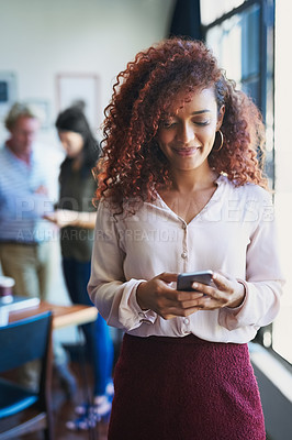 Buy stock photo Shot of a young woman using a mobile phone with her team in the background of a modern office