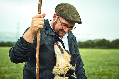 Buy stock photo Shot of a cheerful young farmer and his dog looking at each other while standing on a green field on the farm