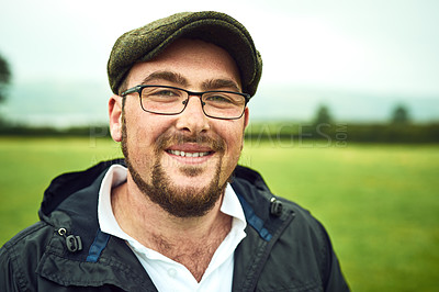 Buy stock photo Portrait of a cheerful young farmer standing on a open green field while looking into the camera outside during the day