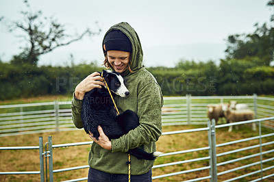 Buy stock photo Shot of a cheerful young farmer holding his young little sheepdog puppy in his arms outside during the day