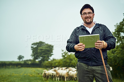 Buy stock photo Portrait of a cheerful young farmer standing with a digital tablet and cane while a flock of sheep grazes in the background